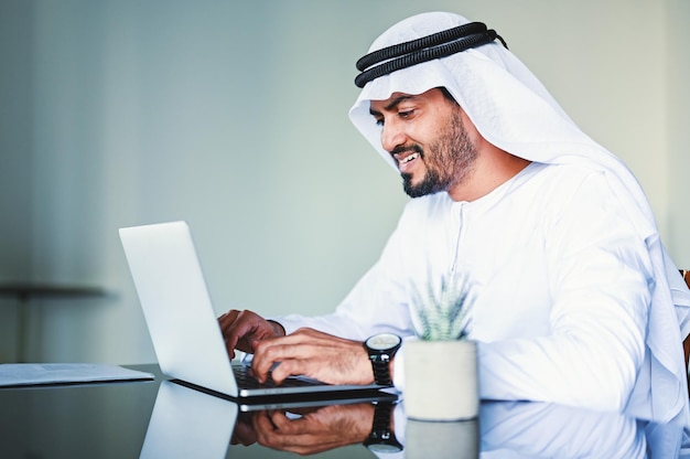 Mężczyzna z bliskowschodnich Emiratów w kandorze pracujący na laptopie z domu