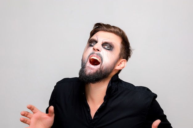 Mężczyzna z brodą i makijażem w stylu nieumarłego na Halloween otworzył usta i pokazuje zęby
