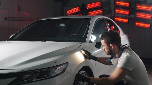 Mężczyzna z brodą i rękawiczkami z latarką jest zajęty sprawdzaniem jakości polerowania karoserii