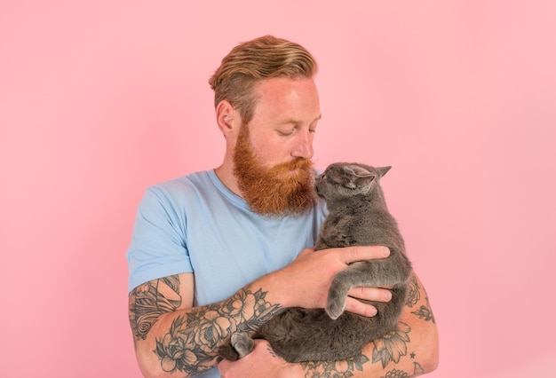 Mężczyzna z brodą i tatuażami pieści szarego kota