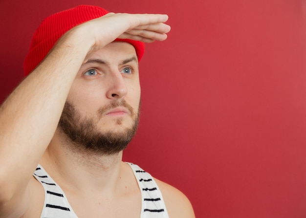 Mężczyzna z brodą w kamizelce i czerwonym kapeluszu spogląda w dal na czerwonym tle
