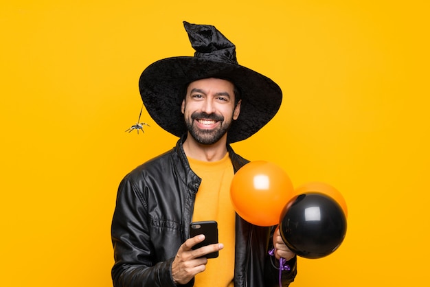 Mężczyzna z czarownica kapeluszem trzyma czarnych i pomarańczowych lotniczych balony dla Halloween przyjęcia wysyła wiadomość z wiszącą ozdobą