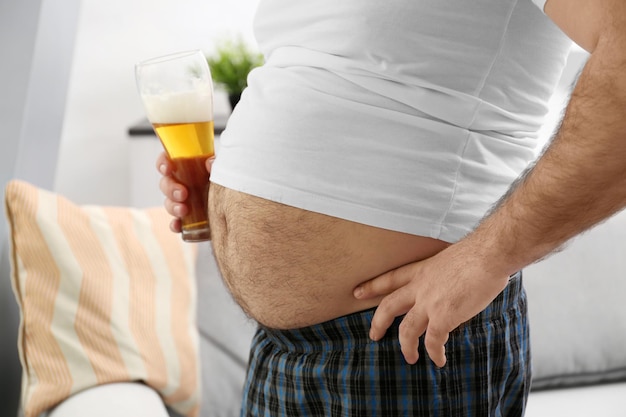 Mężczyzna z dużym brzuchem trzymający szklankę piwa w domu
