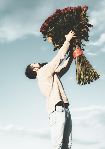 Mężczyzna z dużym bukietem róż Świętuj walentynki i romantyczne prezenty Przystojny facet trzyma bukiet wielkich czerwonych róż Przystojny mężczyzna daje kwiaty swojemu kochankowi w Walentynki