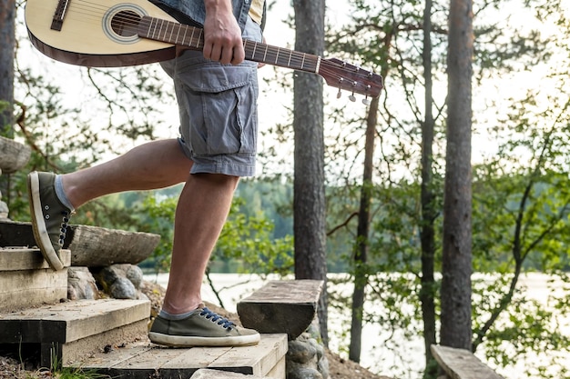 Mężczyzna z gitarą w dłoniach w szortach i tenisówkach schodzi po drewnianych schodach w dół wzgórza