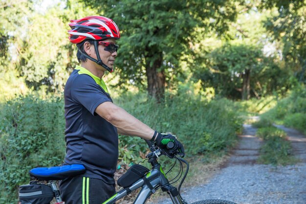 Mężczyzna z hełm rękawiczką dla zbawczej jazdy bicykl przy wsi drogą wzdłuż lasu