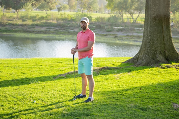 Mężczyzna z klubu golfowego stoi na zielonej trawie trawnika na polu golfowym w ciepły wieczór