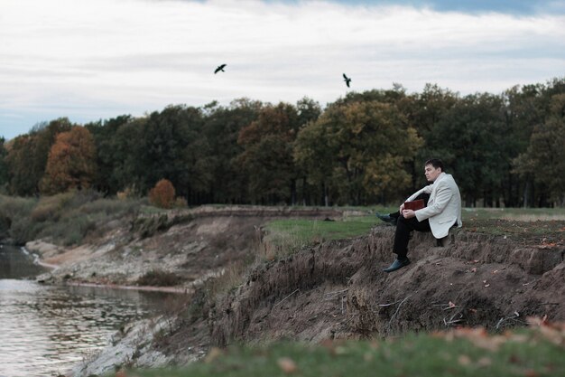 Mężczyzna Z Książką W Rękach Siedzi Na Skraju Urwiska I Wygląda Na Zamyślonego