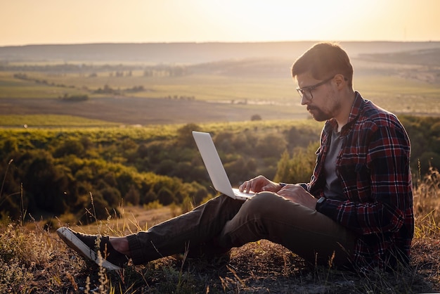 Mężczyzna z laptopem siedzący na skraju góry z przepięknym widokiem na dolinę