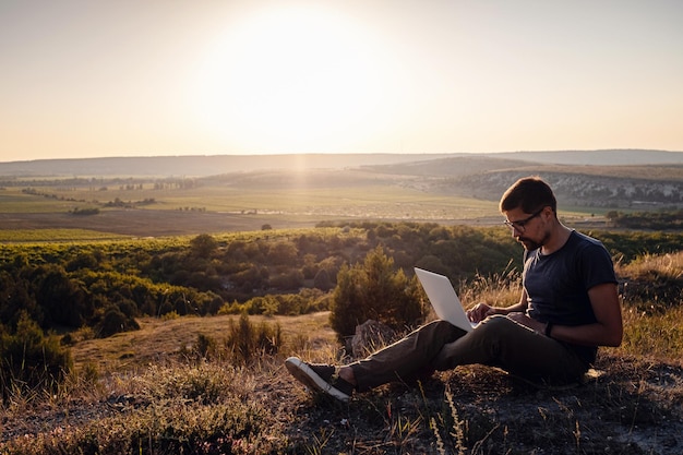 Mężczyzna z laptopem siedzący na skraju góry z przepięknym widokiem na dolinę