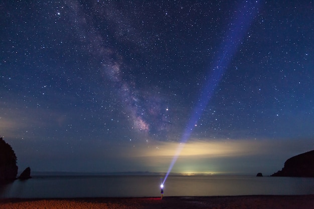 Mężczyzna z latarką patrzący w górę na nocne niebo i Drogę Mleczną