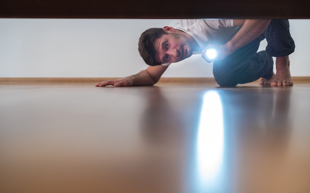 Mężczyzna z latarką zaglądający pod łóżko