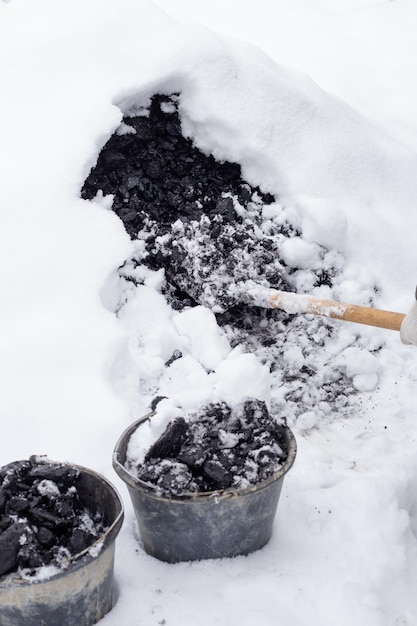 Mężczyzna z łopatą przeszukuje węgiel ze stosu pod śniegiem do wiadra Paliwo do ogrzewania prywatnego domu