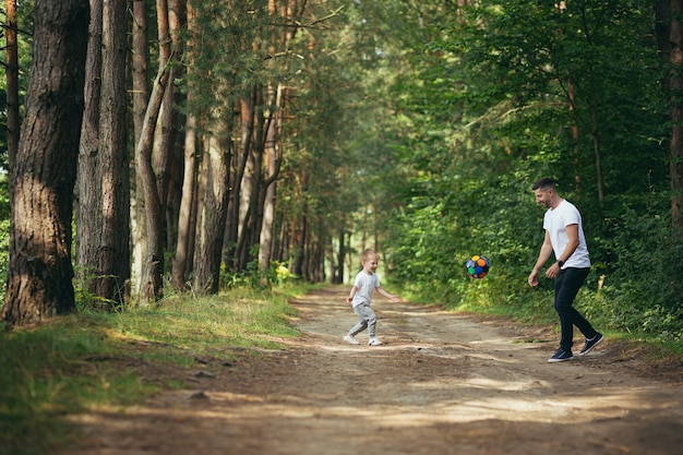 Mężczyzna z małym synkiem grający razem w piłkę nożną kopiący piłkę w lesie spędzają razem czas na zabawie weekend