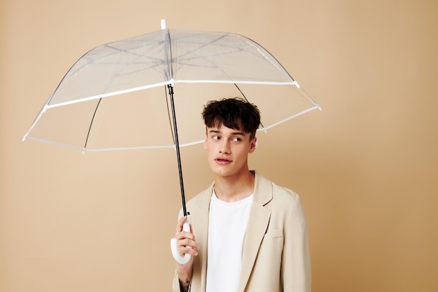 Mężczyzna z otwartym parasolem w kurtce chroniącej przed deszczowym beżowym tłem