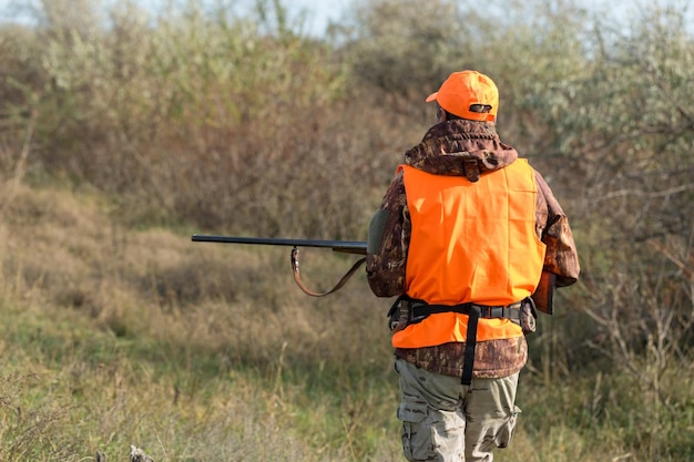 Mężczyzna z pistoletem w rękach i pomarańczową kamizelką na polowaniu na bażanta w zalesionym terenie przy pochmurnej pogodzie Łowca z psami w poszukiwaniu zwierzyny