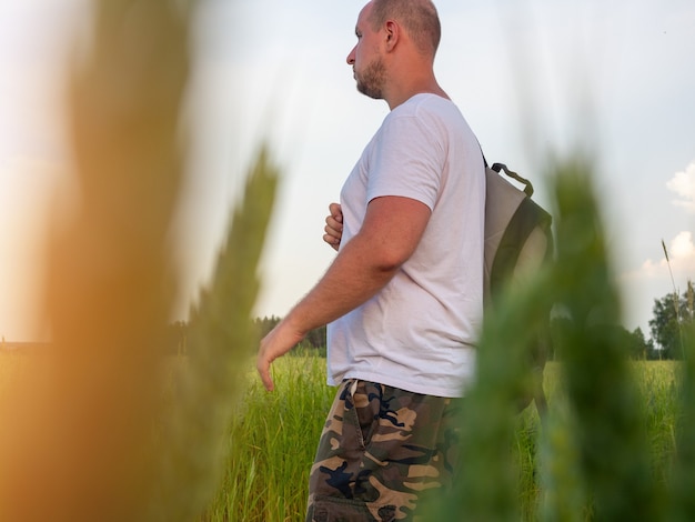 Zdjęcie mężczyzna z plecakiem wychodzi na pole. widok z boku przez trawę. pojęcie wakacji, wolności, podróży