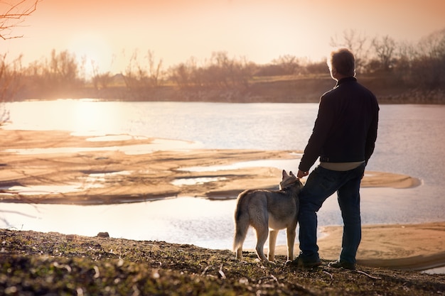 Mężczyzna z psem na brzegu rzeki o zachodzie słońca