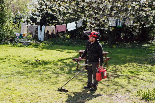 Zdjęcie mężczyzna z ręczną kosiarką ze sprzętem do koszenia trawnika na podwórku