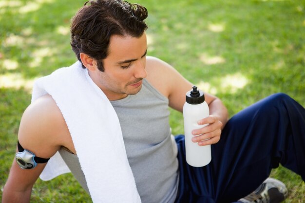 Mężczyzna z ręcznikiem na jego ramieniu patrząc na butelkę sportowych