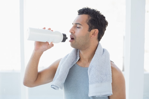 Mężczyzna z ręcznikiem wokoło szyi wody pitnej w sprawności fizycznej studiu