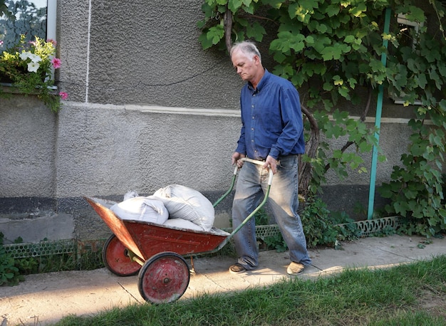 Mężczyzna z taczką pełną worków z cementem w ogrodzie