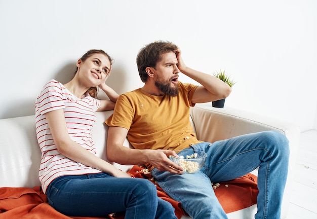 Mężczyzna z talerzami popcorn i kobieta na pomarańczowej kraciastej kanapie przyjaciele rodziny dobrze się bawią Zdjęcie wysokiej jakości