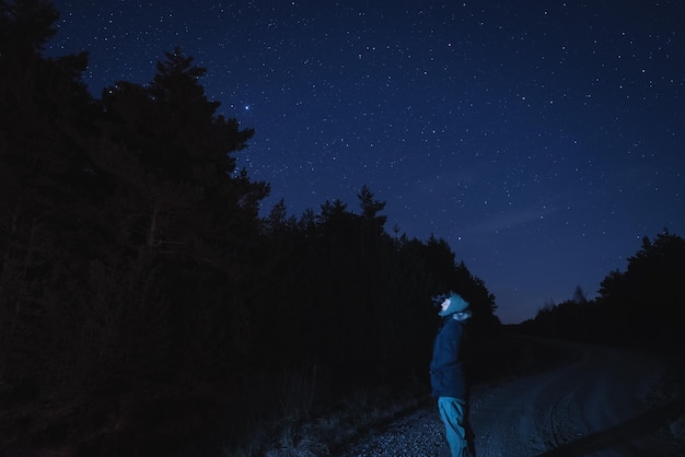 Zdjęcie mężczyzna z urządzeniem nocnego widzenia na głowie w nocy w lesie z gwiezdnym niebem widok boczny