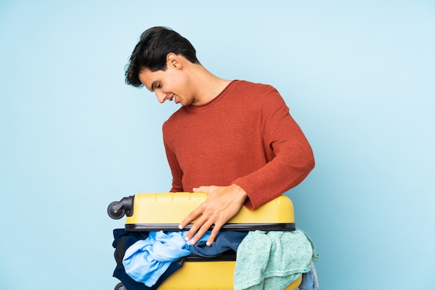 Mężczyzna z walizką pełną ubrań nad odosobnioną błękit ścianą