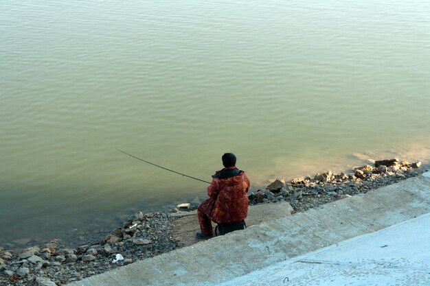 Mężczyzna z wędką siedzi na brzegu rzeki