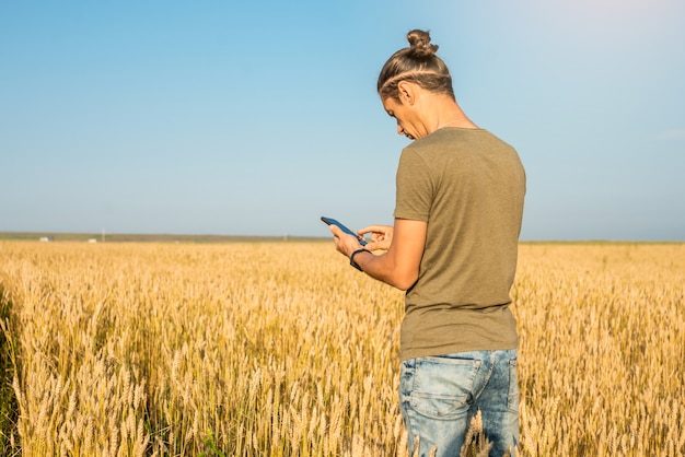 Mężczyzna za pomocą smartfona wśród złotych kłosków pszenicy