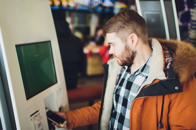 Mężczyzna zamawia jedzenie w terminalu z ekranem dotykowym z elektronicznym menu w restauracji typu fast food.