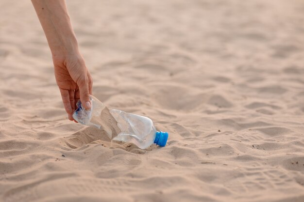Mężczyzna zbiera plastikowe butelki i śmieci na plaży w miejscu publicznym ekologicznym i opiekuńczym