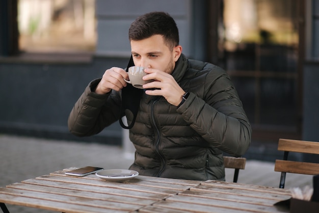 Mężczyzna Zdjął Maskę, żeby Napić Się Cappuccino Na Tarasie. Mężczyzna W Kawiarni Na świeżym Powietrzu Podczas Kwarantanny. Covid19.