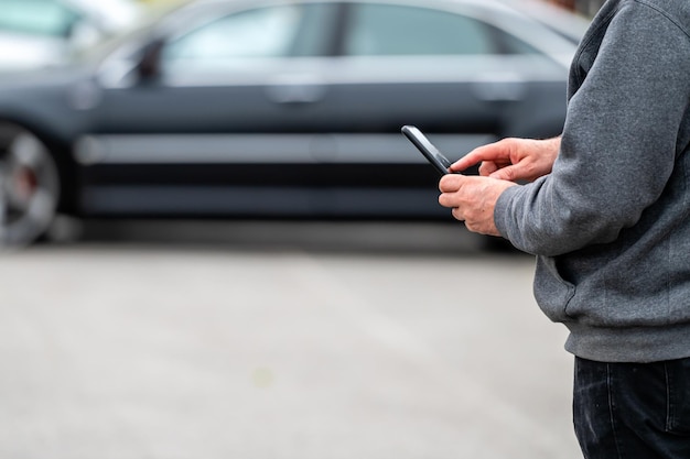 Mężczyzna ze smartfonem stojący obok samochodu, korzystający z aplikacji mobilnej do płacenia za blokadę samochodu lub Internetu