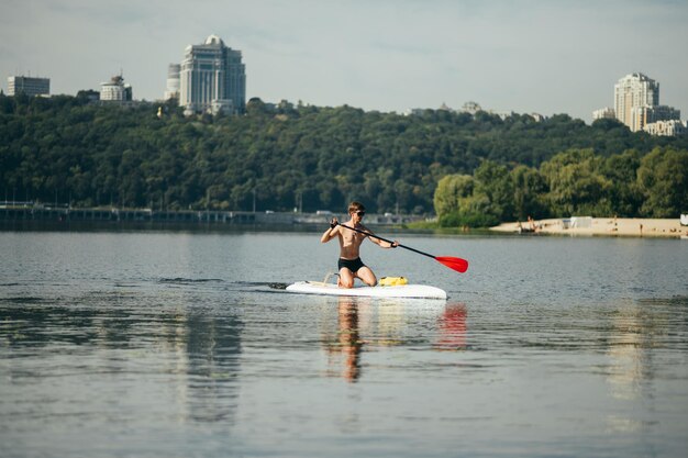 mężczyzna ze sportowym ciałem wiosłuje na desce sup na rzece na tle pięknego krajobrazu