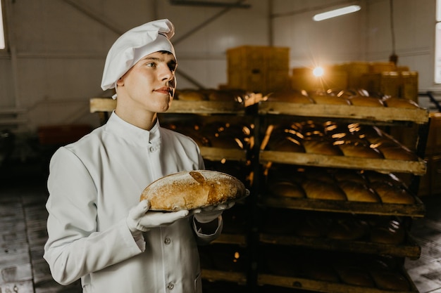 Mężczyzna ze świeżym chlebem w dłoniach piekarz w fartuchu i koszuli dający gorący chleb na czarnym tle