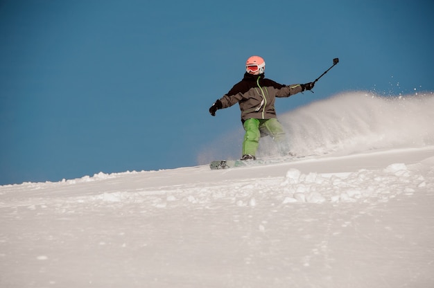 Mężczyzna zjeżdżający ze wzgórza na snowboardzie z aparatem w rękach w popularnym kurorcie turystycznym Gudauri w Gruzji