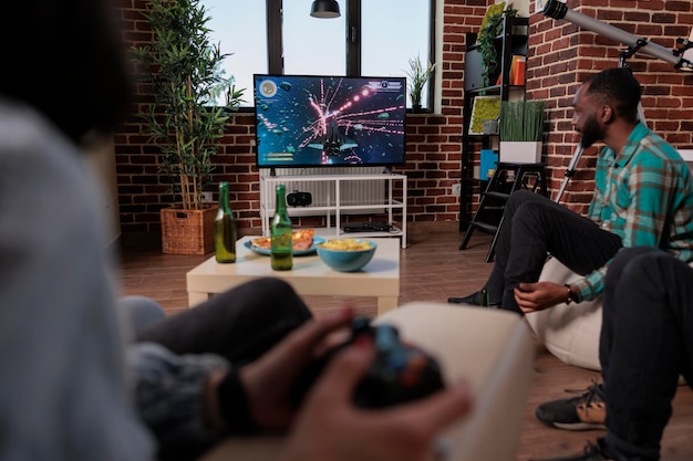 Mężczyźni i kobiety używający konsoli telewizyjnej i joysticka do grania w gry wideo, bawiący się w domu przy butelkach piwa. Grupa ludzi korzystających z zawodów strzeleckich ze strategią gry.