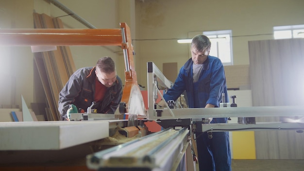 Mężczyźni - stolarze tną drewno piłą elektryczną w fabryce mebli, szeroki widok