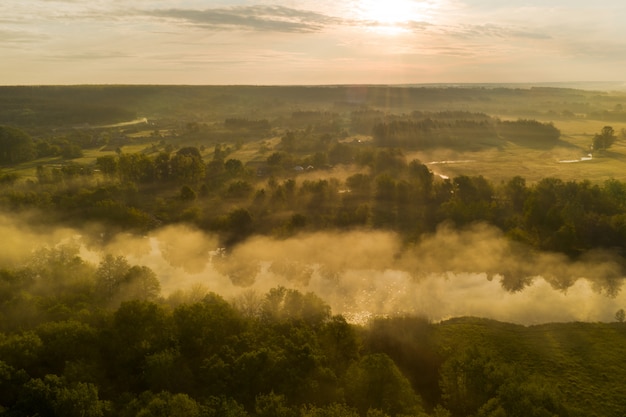 Mgła nad rzeką w pierwszych promieniach świtu słońca wśród lasu w parku przyrody. Pierwsze promienie wschodzącego słońca rozświetlają lekką mgłę nad rzeką.