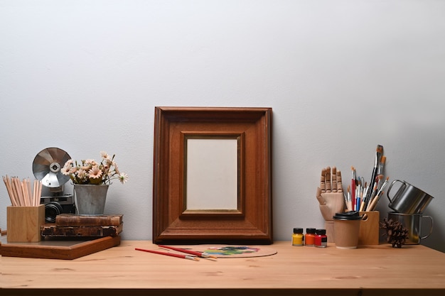 Miejsce pracy artysty z pustą ramką, aparatem i narzędziami do malowania na drewnianym stole.