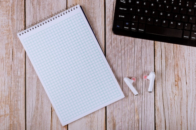 Miejsce pracy z klawiaturą laptopa biurko z papierowym notatnikiem na notatki, słuchawki bezprzewodowe