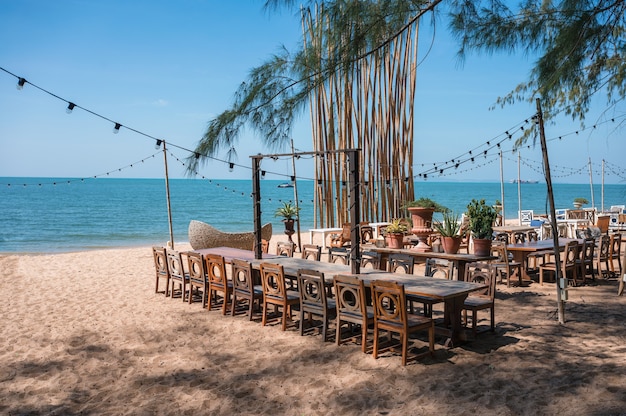 Miejsce uroczystości z drewnianym długim stołem, krzesłem, wiszącą żarówką i dekoracją roślinną w stylu retro na plaży w tropikalnym morzu