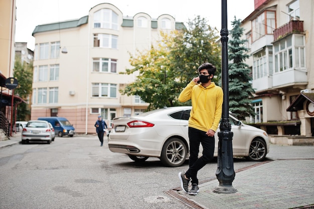 Miejski Młody Indianin Hipster W Modnej żółtej Bluzie Z Telefonem Komórkowym Fajny Facet Z Azji Południowej Nosi Bluzę Z Kapturem I Czarną Maskę Chroniącą Twarz Podczas Nowej Normy