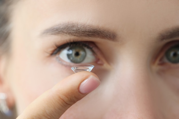 Miękka soczewka kontaktowa na kobiecym palcu na tle kobiecych oczu dopasowana do soczewek jednodniowych