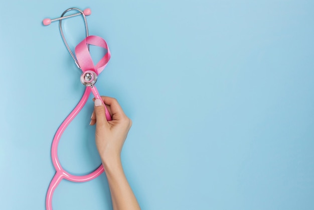 Miesiąc świadomości o raku piersi Ręka trzymająca różową wstążkę i stetoskop