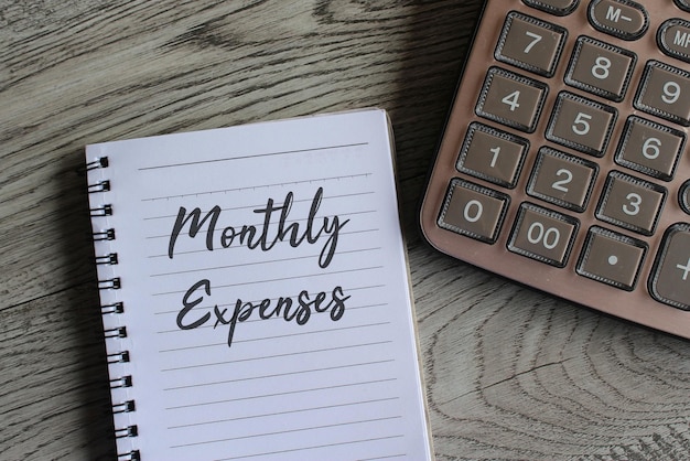 Miesięczne wydatki napisane na notatniku i kalkulatorze na drewnianym stole Pojęcie finansowe