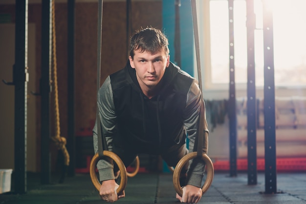 Mięśni ćwiczenia atletyczny mężczyzna robi intensywnemu treningowi przy gym na gimnastycznych pierścionkach.