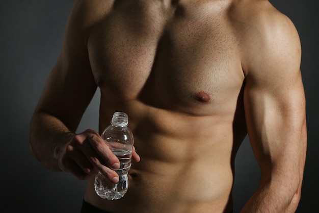 Mięśni młody mężczyzna trzyma butelkę wody na czarno